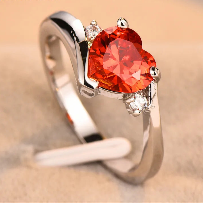 Silver ring with a red heart-shaped gemstone on a beige background