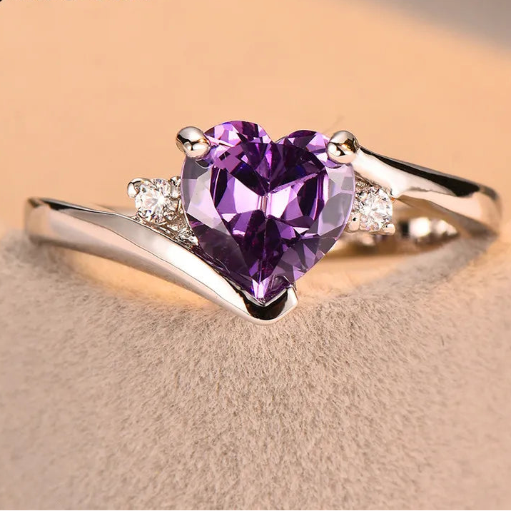 Silver ring with a purple heart-shaped gemstone on a beige background