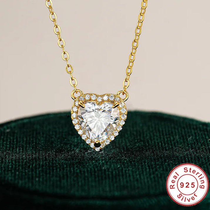 Heart-shaped diamond pendant on a gold chain with 'Real Sterling 925' stamp on a green velvet background.